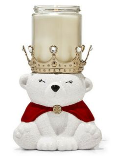 a white teddy bear sitting in front of a candle with a crown on it's head