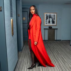 a woman in an orange coat and black shoes is standing in a room with blue walls