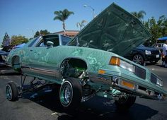 a green car with its hood open in a parking lot