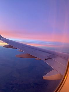 the wing of an airplane as it flies in the sky at sunset or dawn over land and water