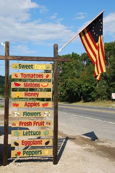 a wooden sign sitting on the side of a road next to a flag and trees