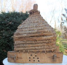 a wooden structure made out of straw sitting on top of a white table next to a bush