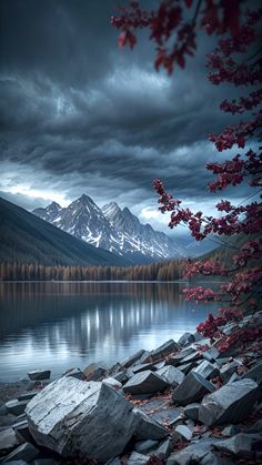 the mountains are covered in red leaves and clouds as they sit next to a body of water