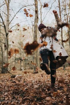 a woman is running through leaves in the woods with her arms up and head down