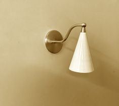 a wall light with a white cone shade on it's side and a beige background