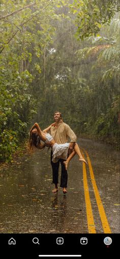 a man and woman dancing in the rain on a wet road with trees behind them