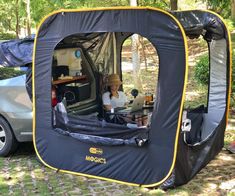 a man sitting in the back of a car next to a tent with its door open