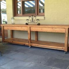 a wooden table sitting on top of a stone floor next to a wall with two windows