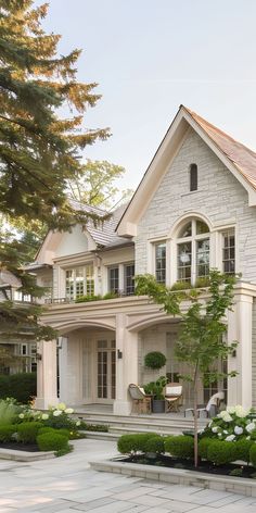 a large white house with lots of windows and plants on the front lawn, surrounded by greenery