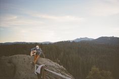 a man sitting on top of a rock next to a forest