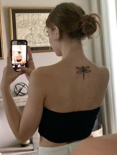 a woman with a dragonfly tattoo on her back taking a selfie in the mirror