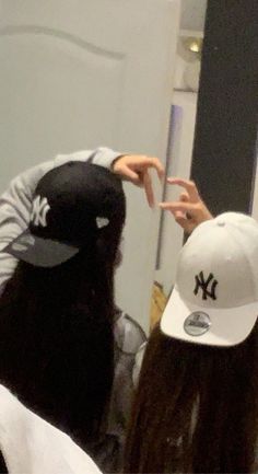 two people in front of a mirror with one pointing at the other's hat