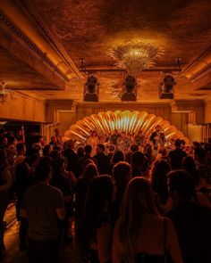 a large group of people standing in front of a stage with an elaborate fan on it