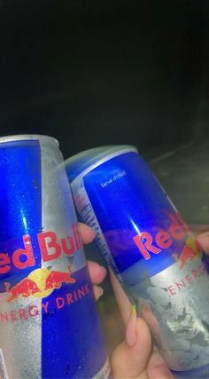 two cans of red bull energy drink being held by someone