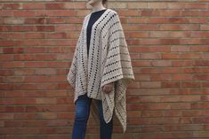 a woman standing in front of a brick wall wearing a crocheted shawl