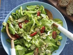 a blue bowl filled with lettuce and tomatoes next to a slice of bread