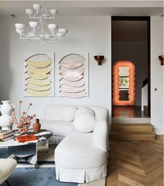 a living room with white furniture and art on the wall