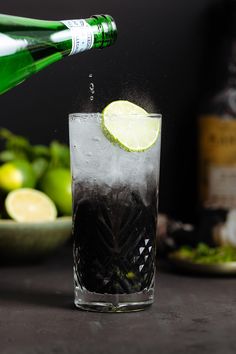 a bottle of alcohol being poured into a glass filled with ice and limes