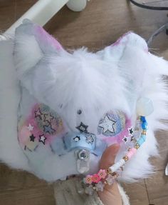 a white teddy bear with pink and blue accessories on it's head is held up to the camera