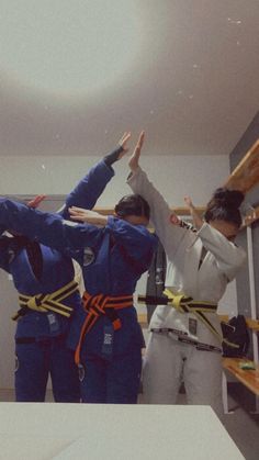 three people in blue uniforms are doing karate moves with their arms up and hands raised