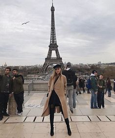 a woman standing in front of the eiffel tower with people walking around her