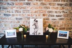 a black table topped with pictures and vases filled with flowers next to a brick wall