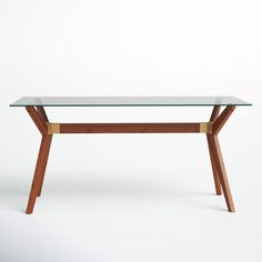 a table with a glass top and wooden legs on a white background in front of a wall