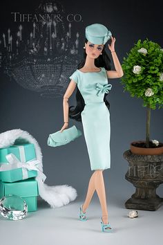 a doll dressed in a blue dress and hat next to a small tree with presents