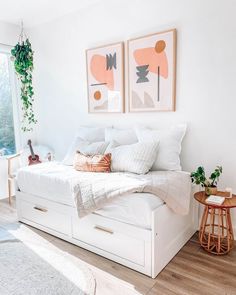 a bedroom with white bedding and two paintings on the wall above it's headboard