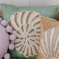 three decorative pillows are sitting on a chair with a pillow in the shape of a seashell