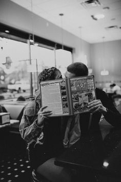 black and white photograph of two people sitting at a table reading a book in a restaurant