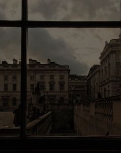 the view from an open window shows people walking on a bridge and buildings in the distance