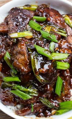 a white plate topped with meat covered in sauce and green onions on top of rice