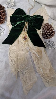 a green bow tied on top of lace next to pine cones