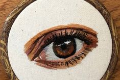 an eye painted on a wooden frame with white and brown thread in the center, sitting on a table