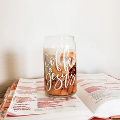 an open book on top of a table next to a glass filled with coffee beans