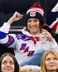 a woman sitting in the stands at a hockey game wearing a new york rangers hat