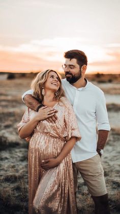 a man and woman are standing together in the desert at sunset with their arms around each other