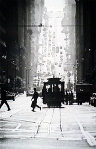 a black and white photo of people crossing the street in front of a trolley car