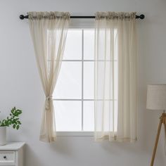 a window with sheer curtains hanging from it's side and a lamp next to it