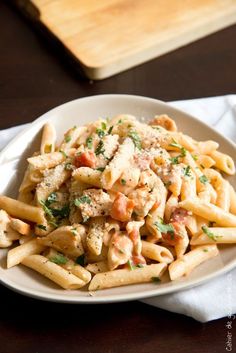 pasta with chicken and parmesan cheese on a white plate next to a wooden cutting board