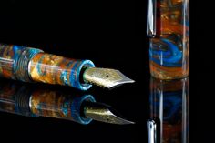 two fountain pens sitting next to each other on top of a black surface with reflections