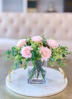 pink roses and greenery in a glass vase on a marble tray