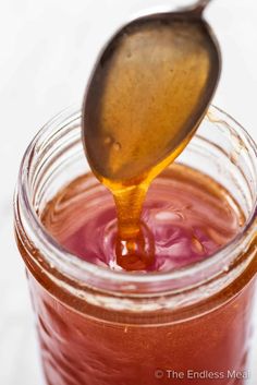 a spoon is pouring honey into a jar