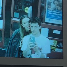 a man and woman standing in front of a store window looking at a cell phone