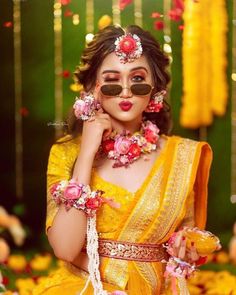 a woman in yellow dress with flowers around her neck and sunglasses on, posing for the camera