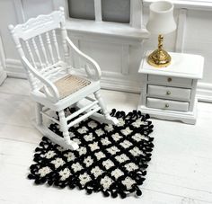 a white rocking chair sitting next to a black and white rug on top of a floor