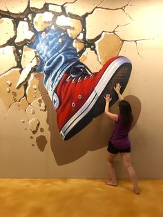 a woman standing in front of a wall with an image of a pair of shoes on it