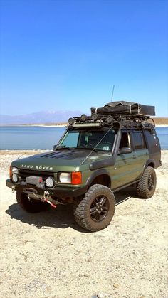 an suv is parked on the beach with its roof rack and luggage strapped to it