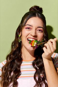 a woman holding a spoon full of food to her mouth and smiling at the camera